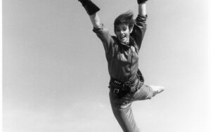 Black and white image of Pat leaping into the air with a sword during her stuntwoman days.